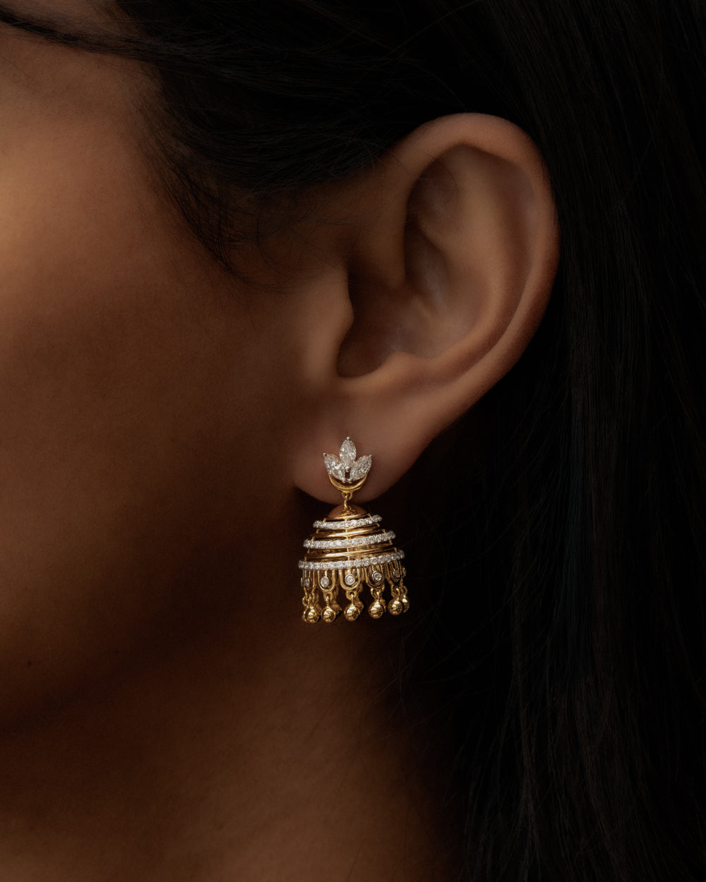 Gold earring worn by a person with a dark background